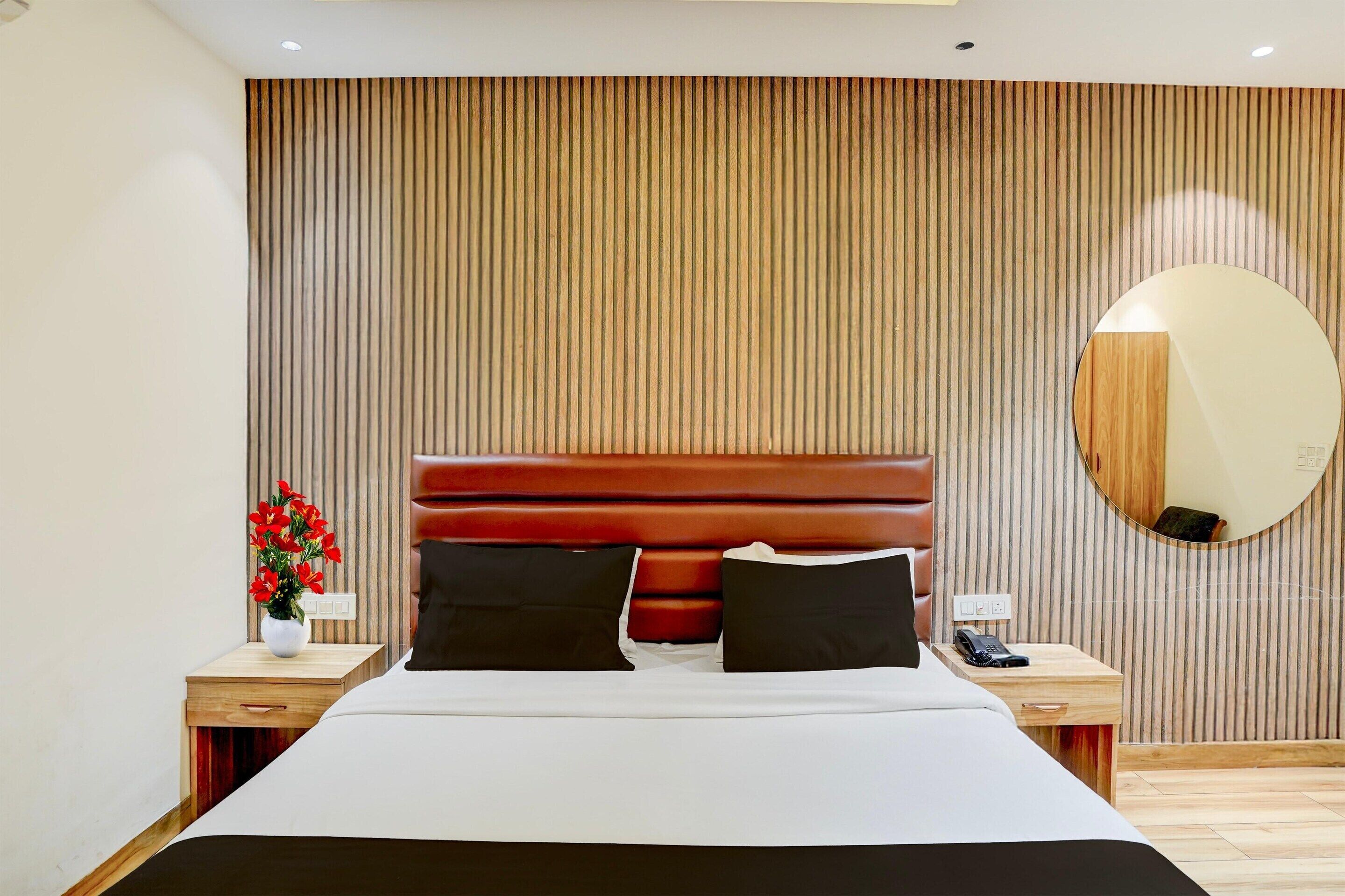 Moderni hotellihuone, jossa on suuri sänky, puupanelilla verhoiltu seinä ja pyöreä peili.