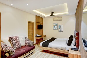 Una habitación de hotel moderna con una cama, un sofá, un televisor y un ventilador de techo.