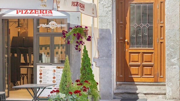 Una pizzeria con posti a sedere all'aperto, una bacheca con il menù e un'esposizione di fiori davanti.