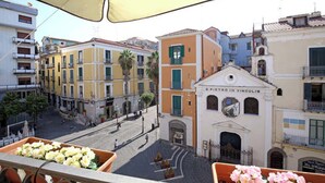 Una vista di una strada con edifici, un cartello con la scritta 'Piazza in Vignellis' e un'esposizione di fiori su un balcone.