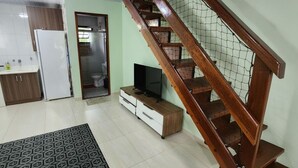 Ein Wohnzimmer mit einer Holztreppe, einem Fernseher auf einem Holzboden, einer Küchenzeile und einem gemusterten Teppich.