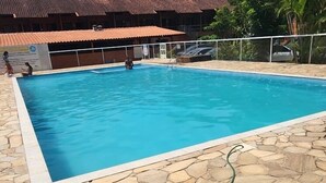 Ein Schwimmbecken mit Steinböden, einem eingezäunten Bereich und einem Gebäude mit rotem Dach im Hintergrund.