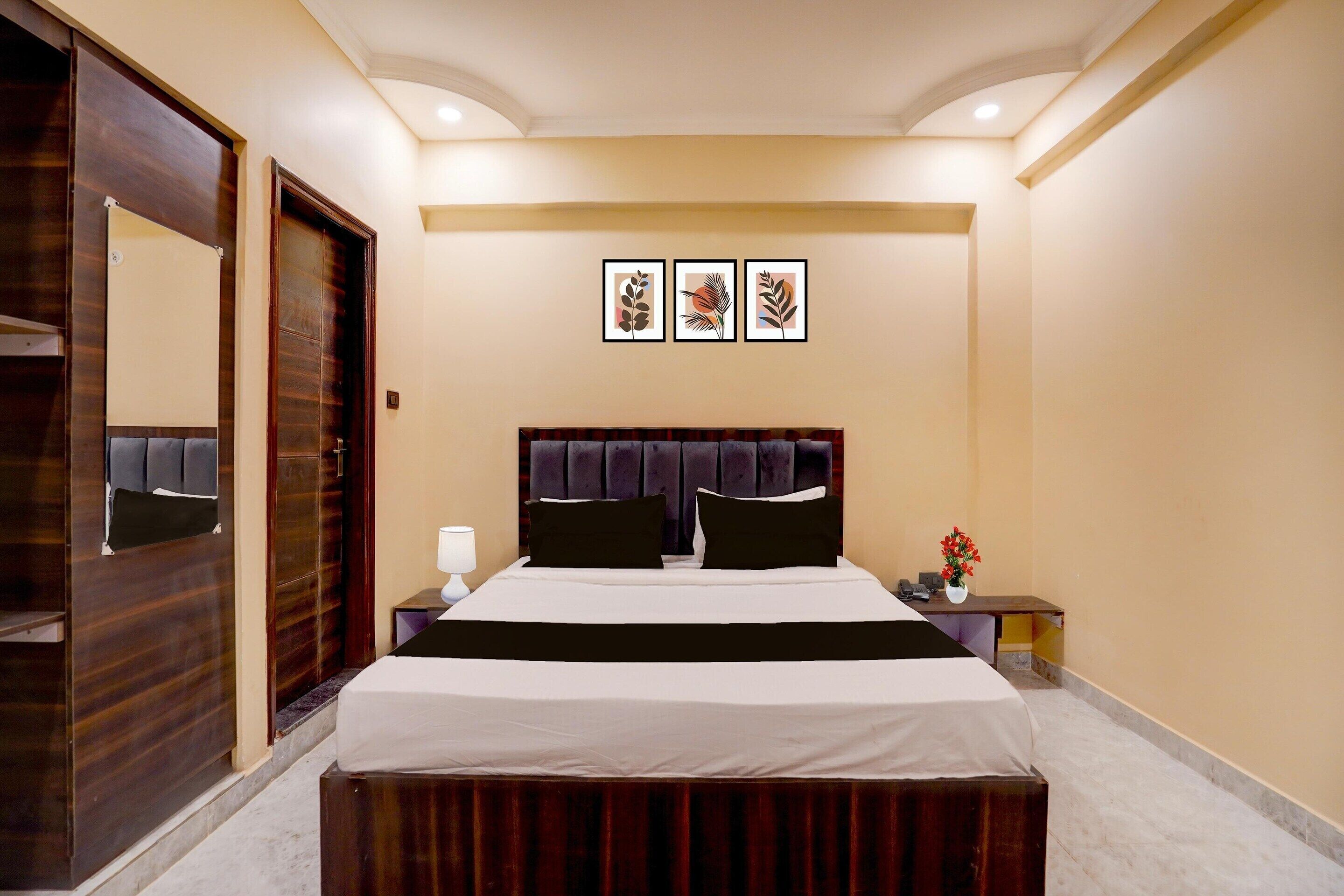 A hotel room with a bed, a nightstand, a mirror, and framed artwork on the wall.