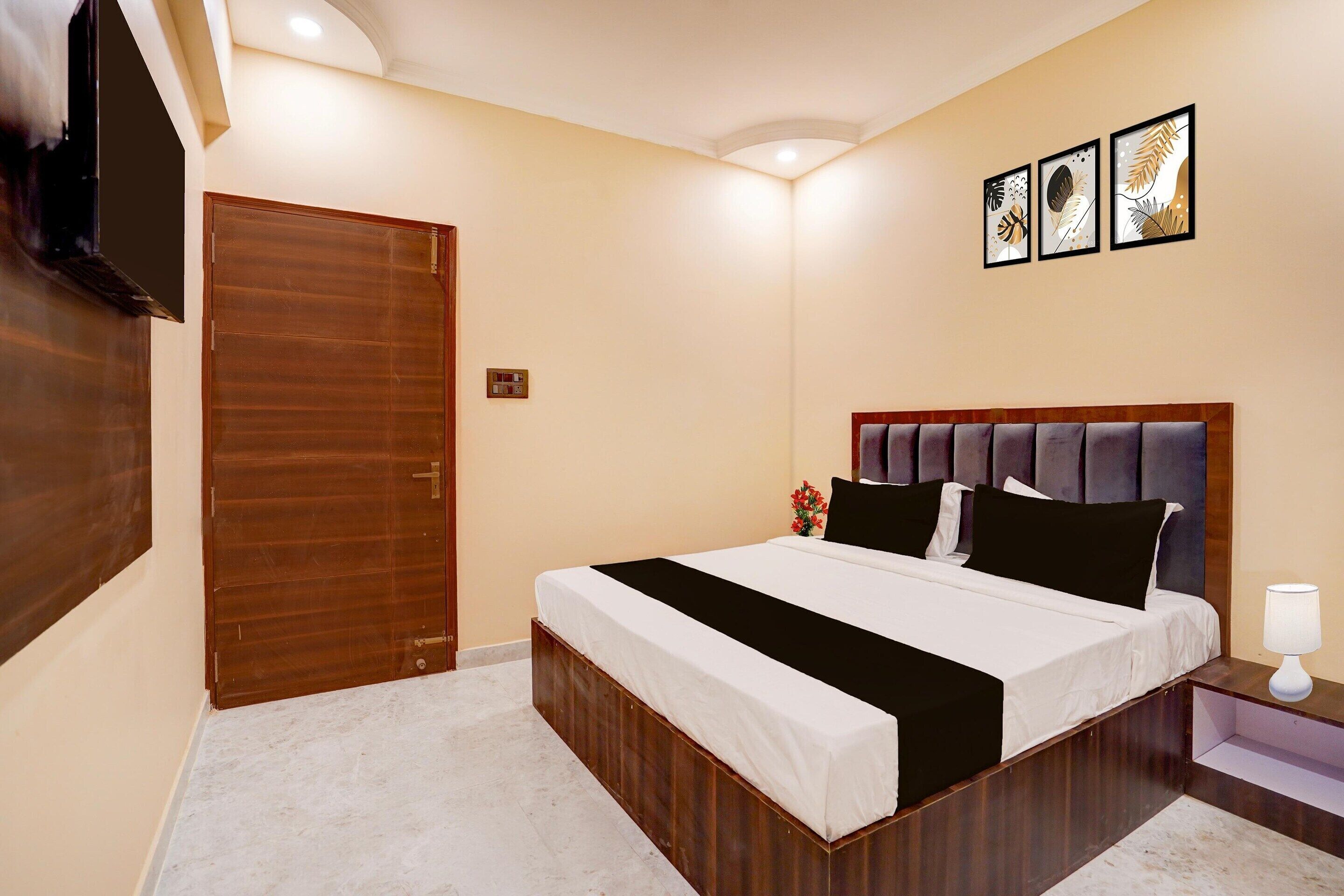 A hotel room with a wooden bed frame, a flat-screen TV, and three framed artworks on the wall.