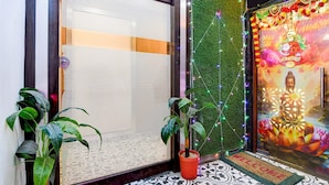 A room with a closed sliding door, a green wall with a decorative string of lights, a Buddha mural, and two potted plants. - Suite Marquis Street BK International (Kolkata)