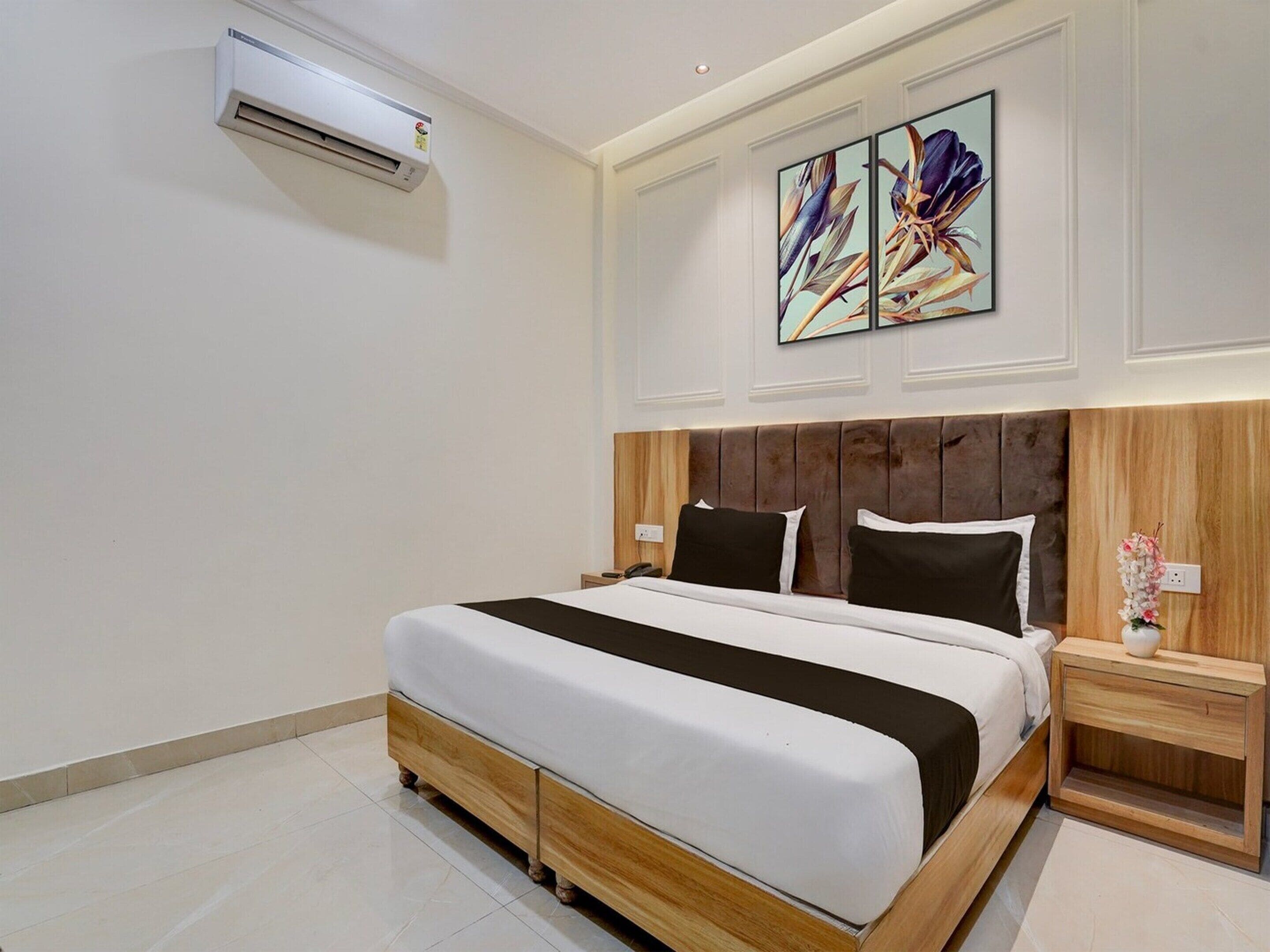 Une chambre d’hôtel moderne avec un grand lit, une tête de lit en bois, des murs blancs et un tableau au-dessus du lit.