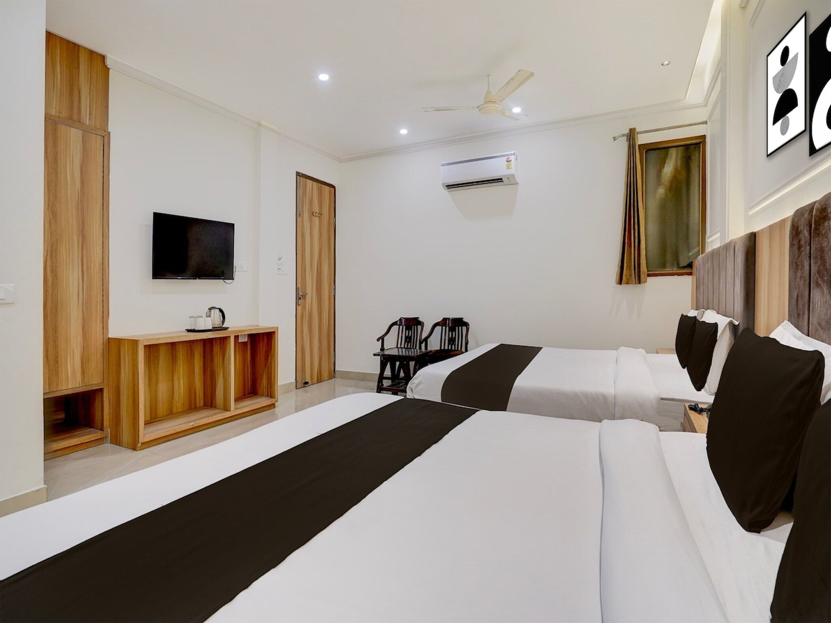 A hotel room with two beds, a TV, a ceiling fan, and a window with curtains.