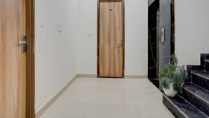 A hallway with a wooden door, a potted plant, and a staircase with black tiles. - Deluxe With Twin Bedram Talai Crossway (Amritsar)