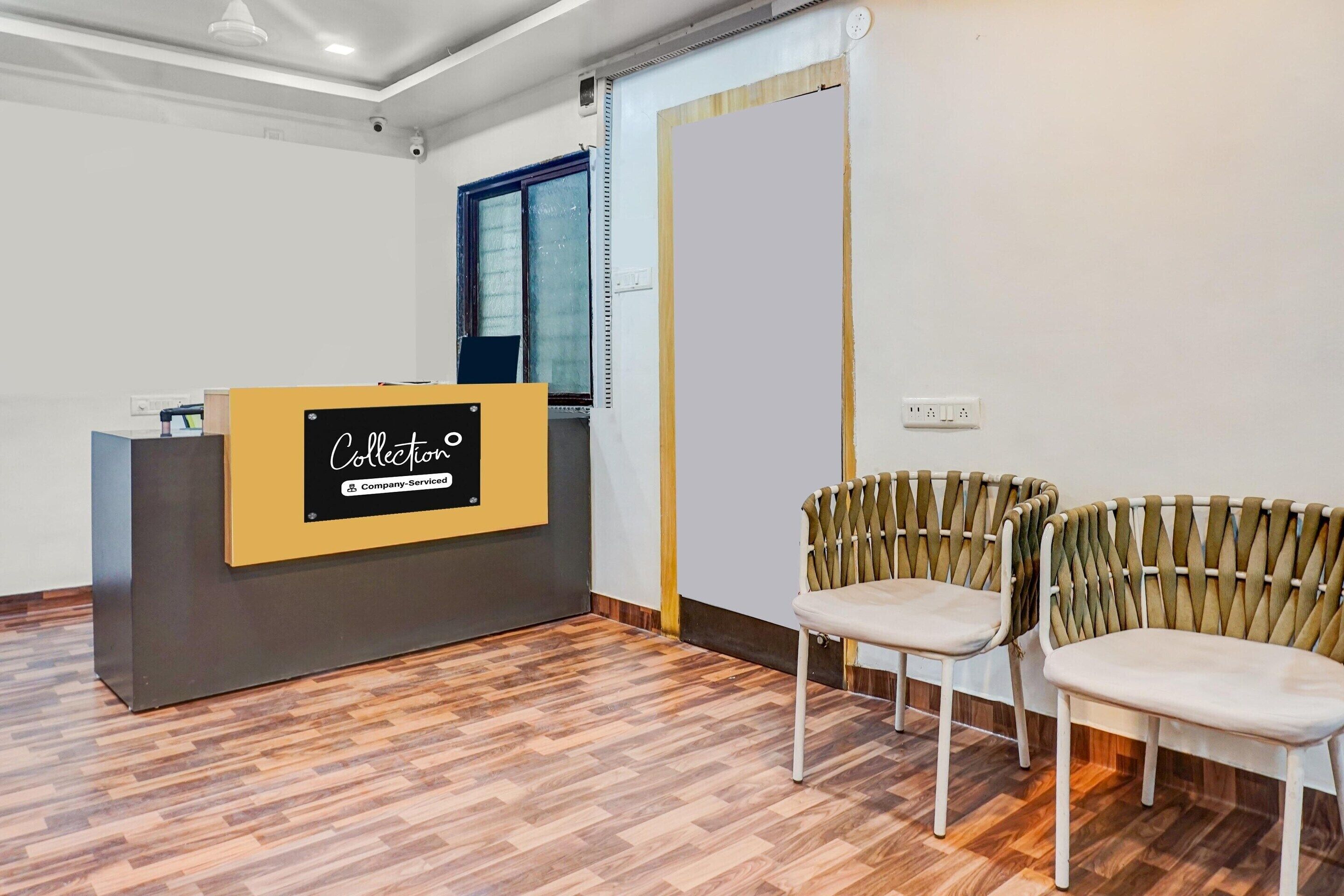 A reception desk with a sign reading 'Collection Company-Serviced' in a room with wooden flooring and two upholstered chairs.