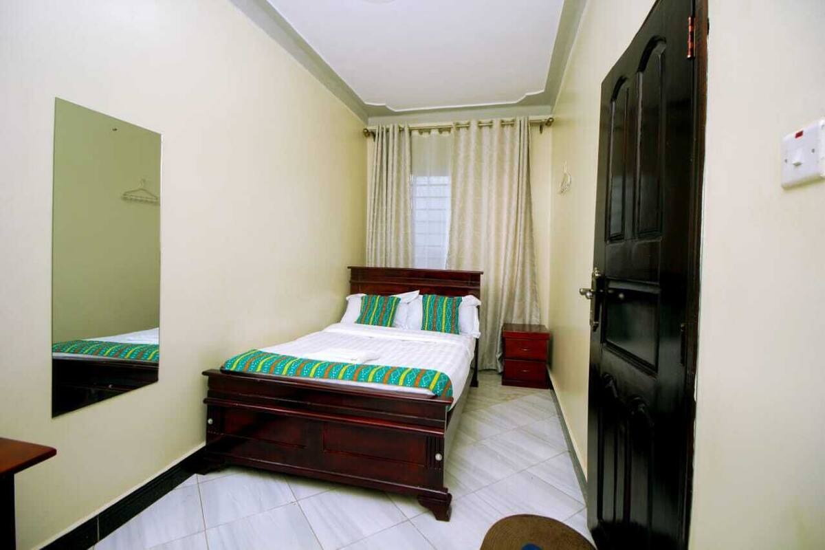 A bedroom with a bed, a dresser, a mirror, a door, and a window with curtains.