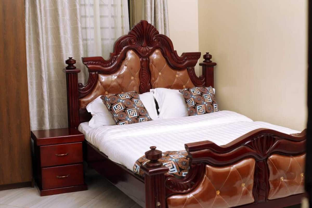 A wooden bed with a tufted headboard, two pillows with geometric patterns, a white bedspread, and a wooden nightstand with drawers.