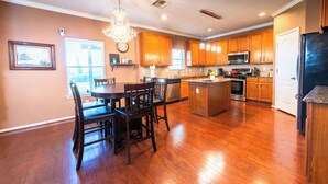 A spacious kitchen with wooden cabinets, a dining area with a table and chairs, and a large island with a sink. - 3-Bdrm, 2.5-Bth WaterFront View Home (Katy)