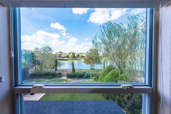 A window with a view of a lake, trees, and a grassy area.