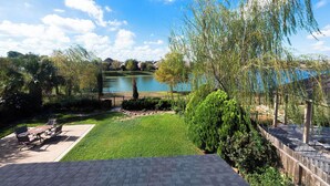Une terrasse avec des meubles d’extérieur, une pelouse et une vue sur un lac, avec des maisons en arrière-plan.