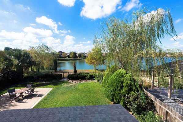 A patio with outdoor furniture, a grassy area, and a view of a lake with houses in the background. - 3-Bdrm, 2.5-Bth WaterFront View Home (Katy)