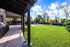 Un patio techado con una parrilla, césped y vistas a un barrio residencial.