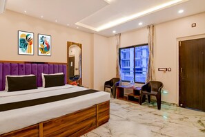 Habitación de hotel con cama, escritorio, silla, ventana con vistas y obras de arte en la pared.