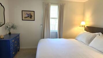 A bedroom with a bed, a dresser, a lamp, a window with curtains, and a framed picture on the wall.