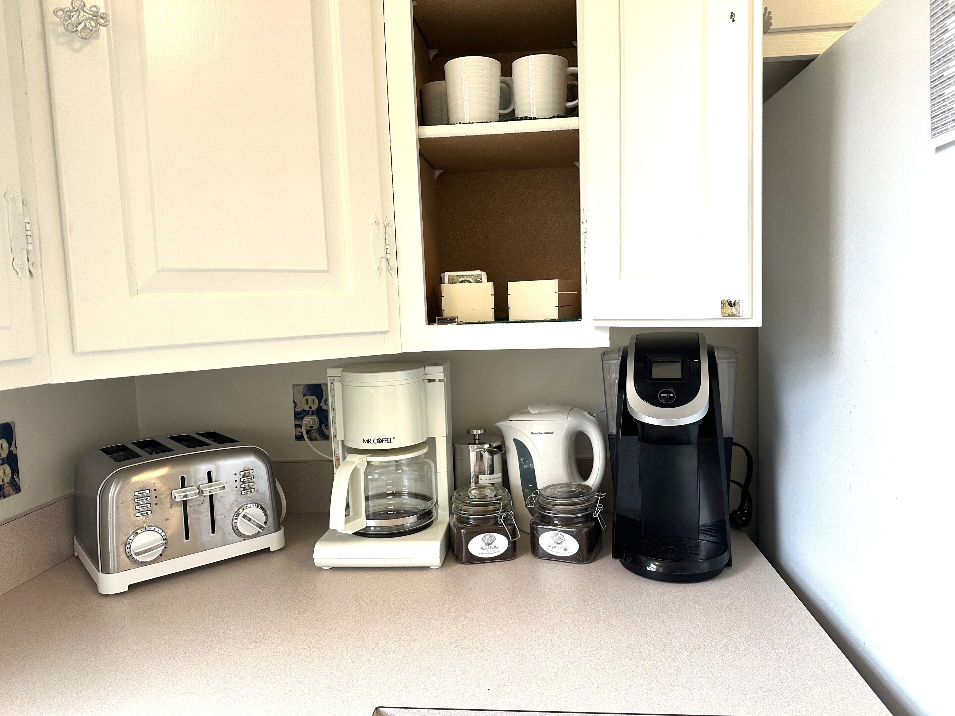 A kitchen with a toaster, a coffee maker, a kettle, and jars on the counter.