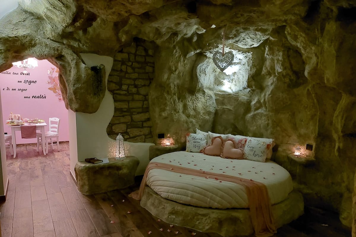 A cave-like bedroom with a bed, a small table with chairs, and a stone wall.