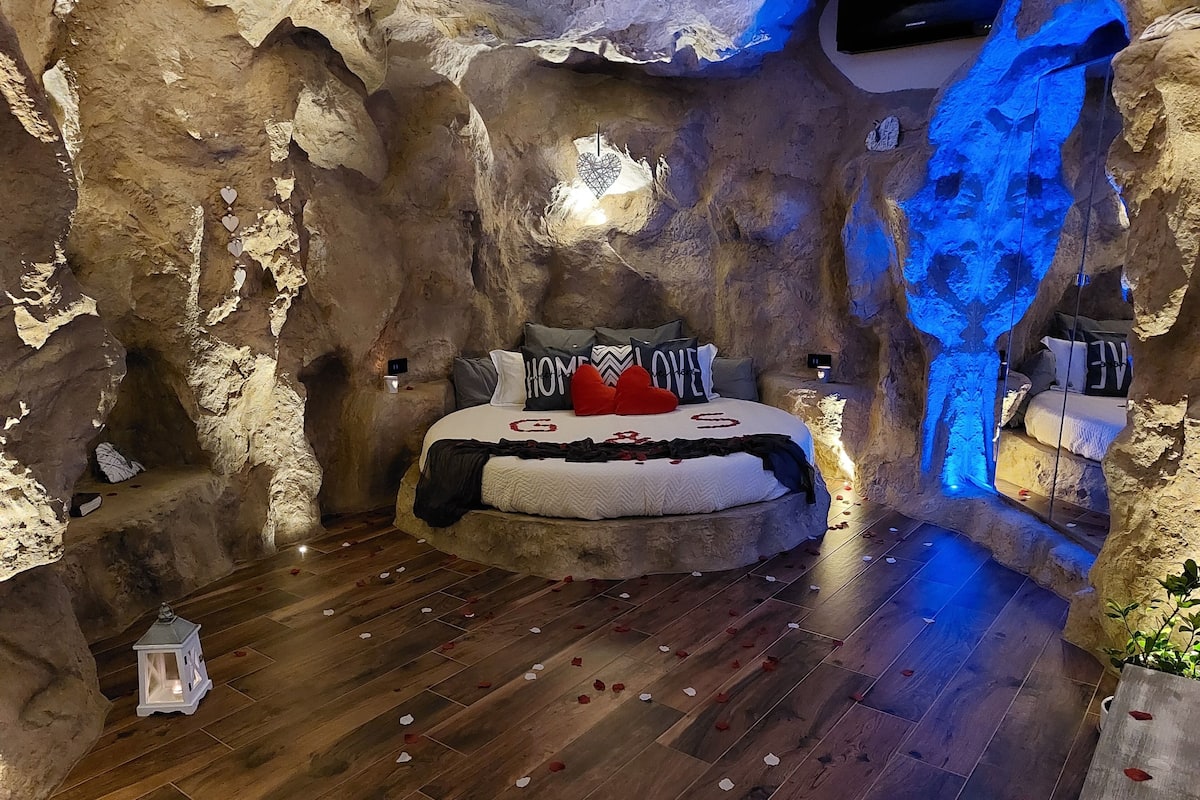 A room with a bed, a nightstand, a wall-mounted TV, and a decorative wall feature.