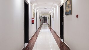 Un largo pasillo bien iluminado, con paredes blancas, suelo de mármol y puertas a ambos lados.