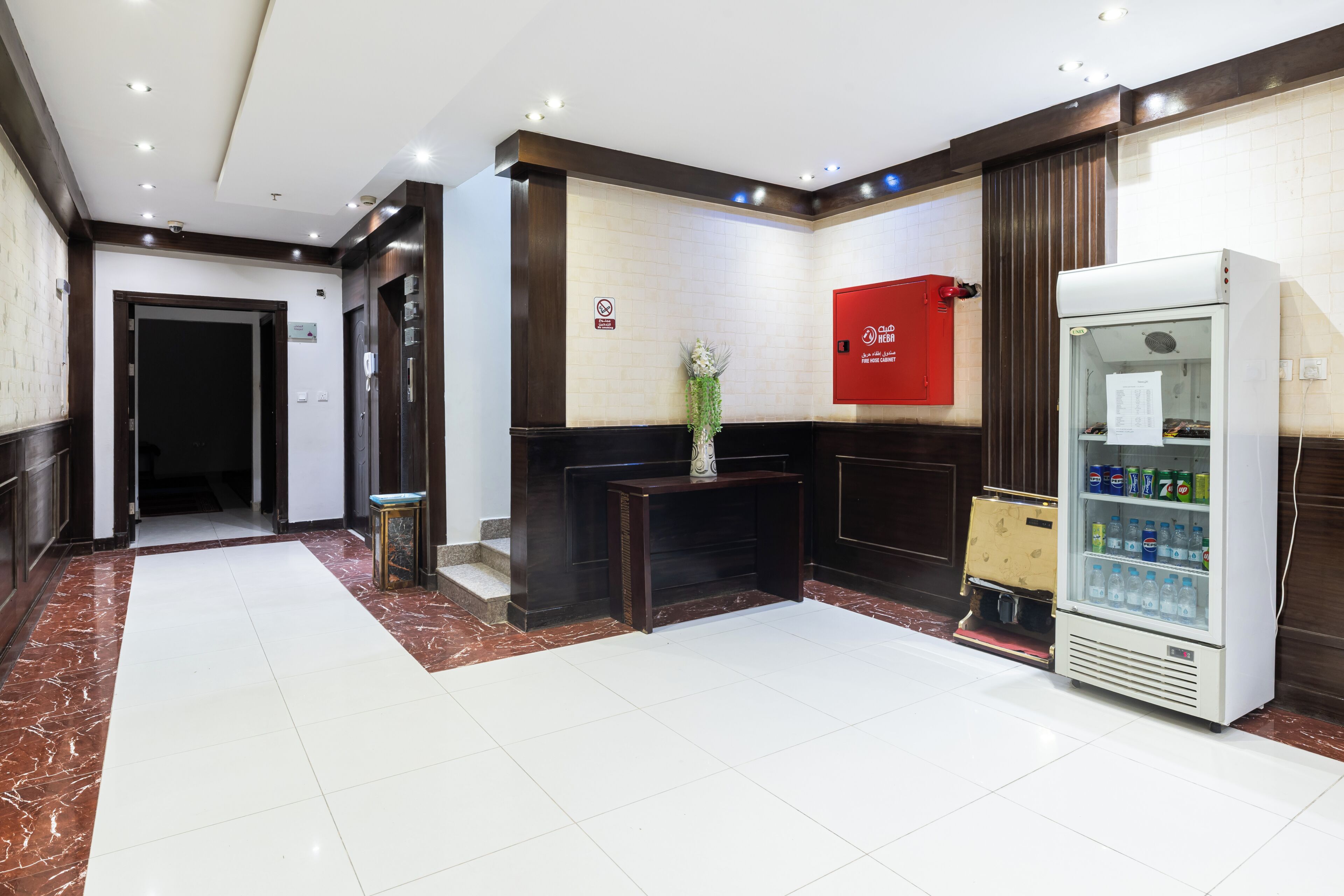 Ein Hotel-Empfangsbereich mit Marmorboden, einem roten Schild, einem Automaten und einer Tür zu einem weiteren Raum.