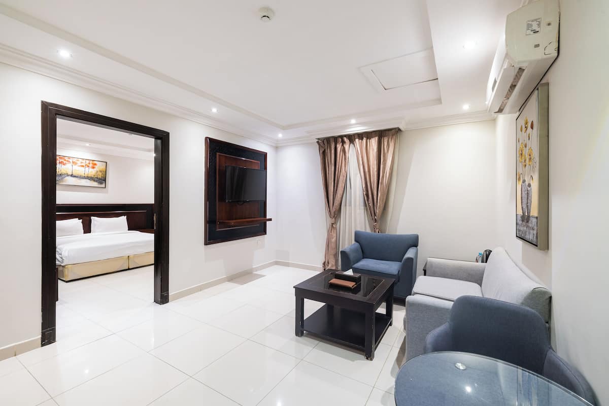 Quarto de hotel com cama, televisão presa à parede, sofá, mesa de centro e um quadro na parede.