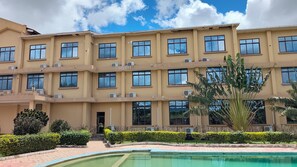 A multi-story building with a swimming pool, air conditioning units, and a well-maintained garden. - The Royal Ambassador Hotel (Dodoma)