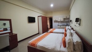 Habitación de hotel con dos camas, televisión, escritorio y kitchenette.