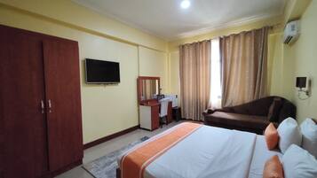 Habitación de hotel con cama, escritorio con silla, televisión, armario y sofá.