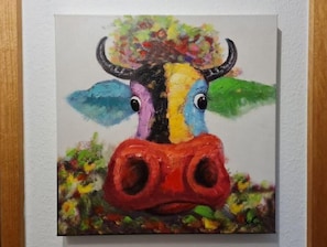 Un tableau représentant un taureau aux couleurs vives, avec un nez rouge et des cornes, entouré de feuillage verdoyant.