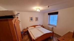 Un dormitorio con una cama de madera, una mesita de noche, un aparador y una ventana con cortinas.