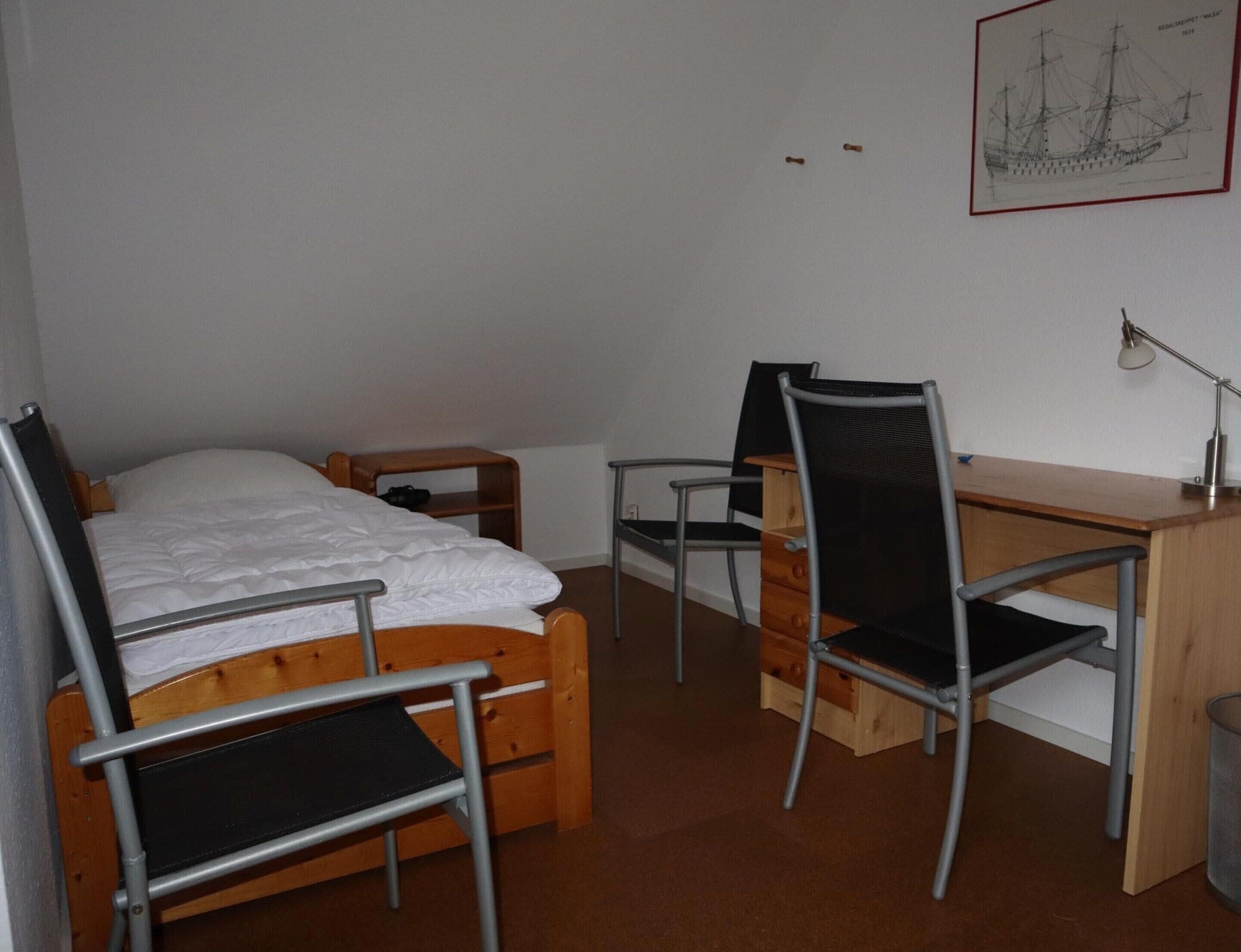 A bedroom with a bed, a desk, two chairs, and a wall-mounted lamp.