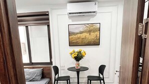 A room with a bed, a table with chairs, an air conditioning unit, and a painting on the wall. - Era Hong Mai Apartment (Hanoi)