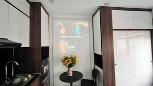 A compact kitchen with a sink, a small table with a vase of flowers, and a projection screen displaying text. - Era Hong Mai Apartment (Hanoi)