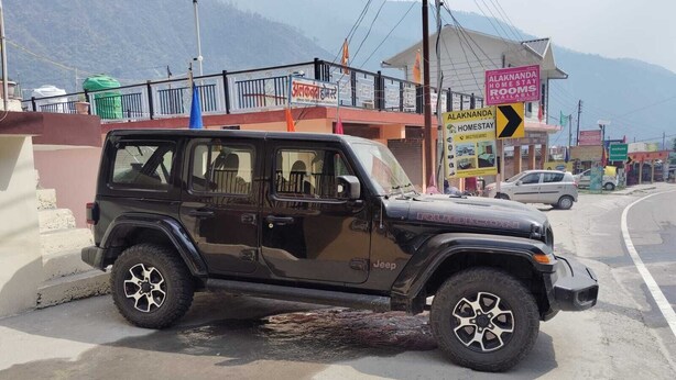 Ein schwarzer Jeep steht auf einer Straße, im Hintergrund ist ein Schild für Alaknanda Homestay zu sehen.