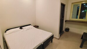 Ein Schlafzimmer mit Bett, Nachttisch, kleinem Tisch, Stuhl und Fenster mit Blick ins Freie.