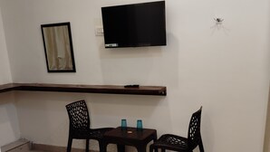 Ein Hotelzimmer mit Bett, Wandfernseher, einem kleinen Tisch mit Stühlen und einem Regal darüber.