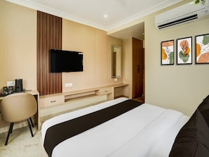 A hotel room with a bed, a desk with a chair, a flat-screen TV, a mirror, and artwork on the wall.