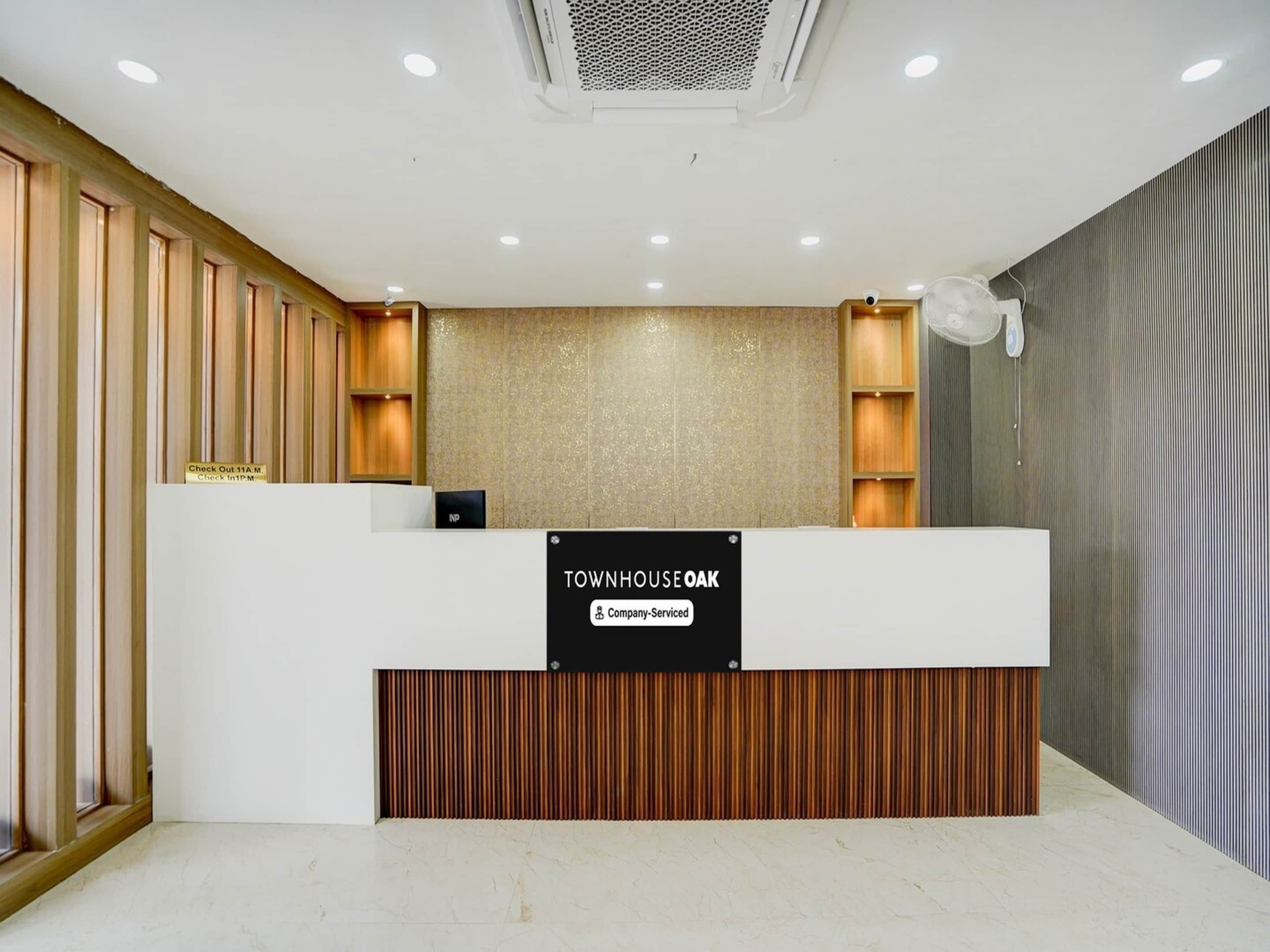 A reception desk with a sign indicating it is company-serviced, wooden paneling on the walls, and a ceiling with recessed lighting.