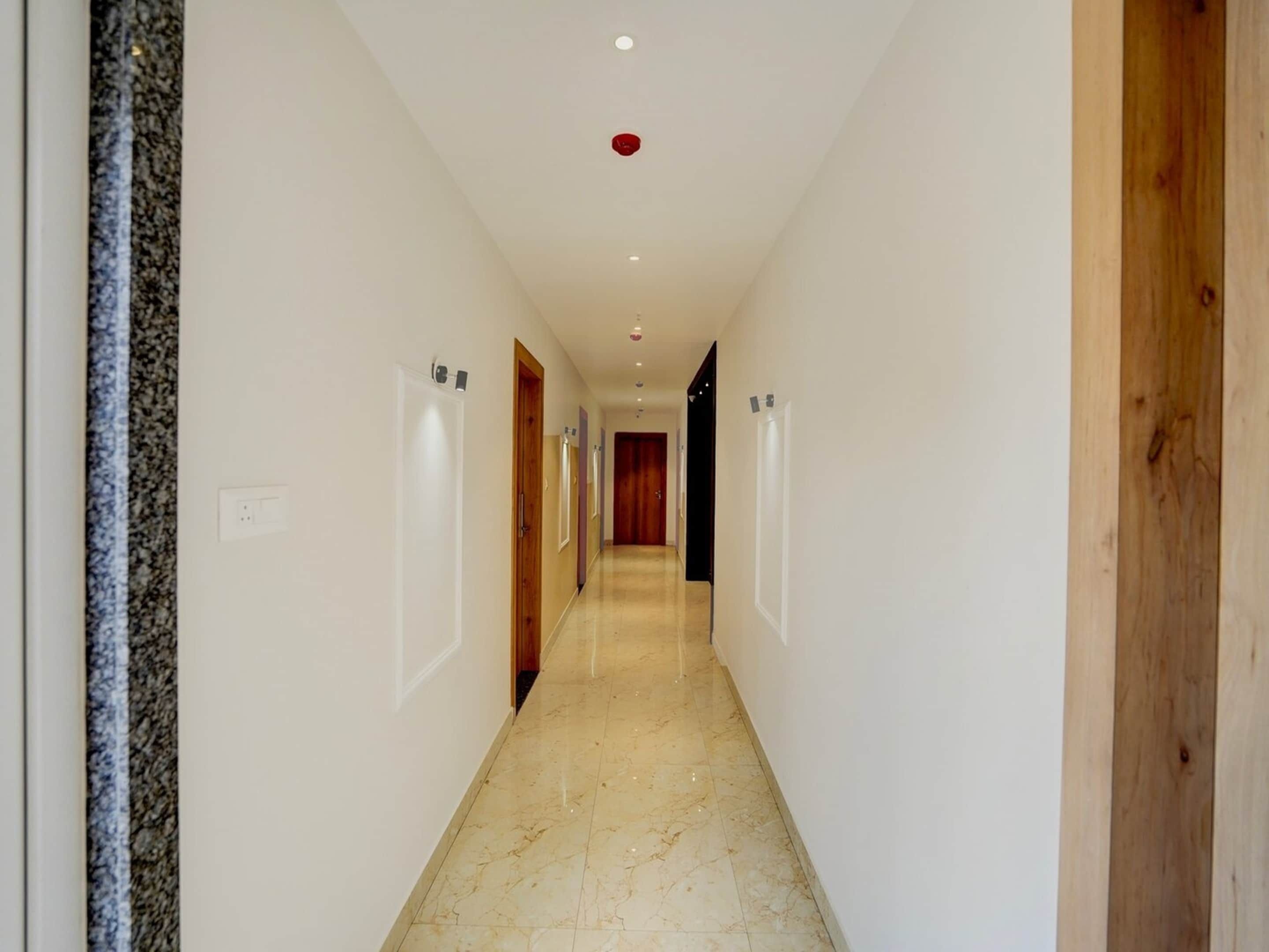 A hallway with white walls, a marble floor, and wooden doors.