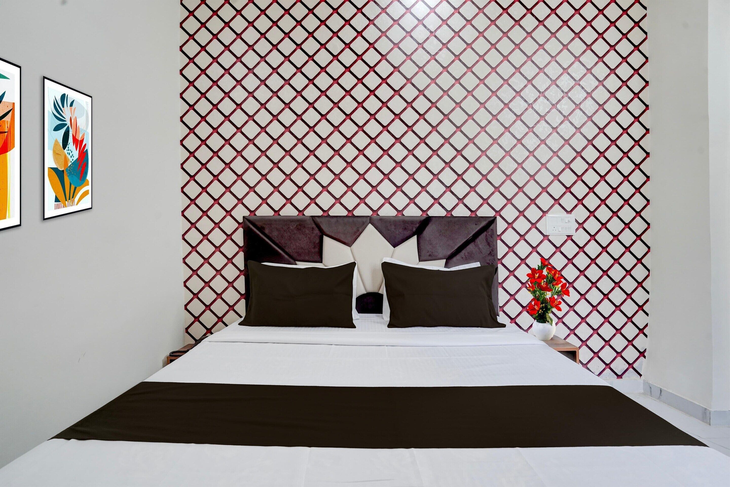Quarto de hotel moderno com uma cama, cabeceira decorativa, mesa de cabeceira, um vaso com flores e duas obras de arte emolduradas na parede.