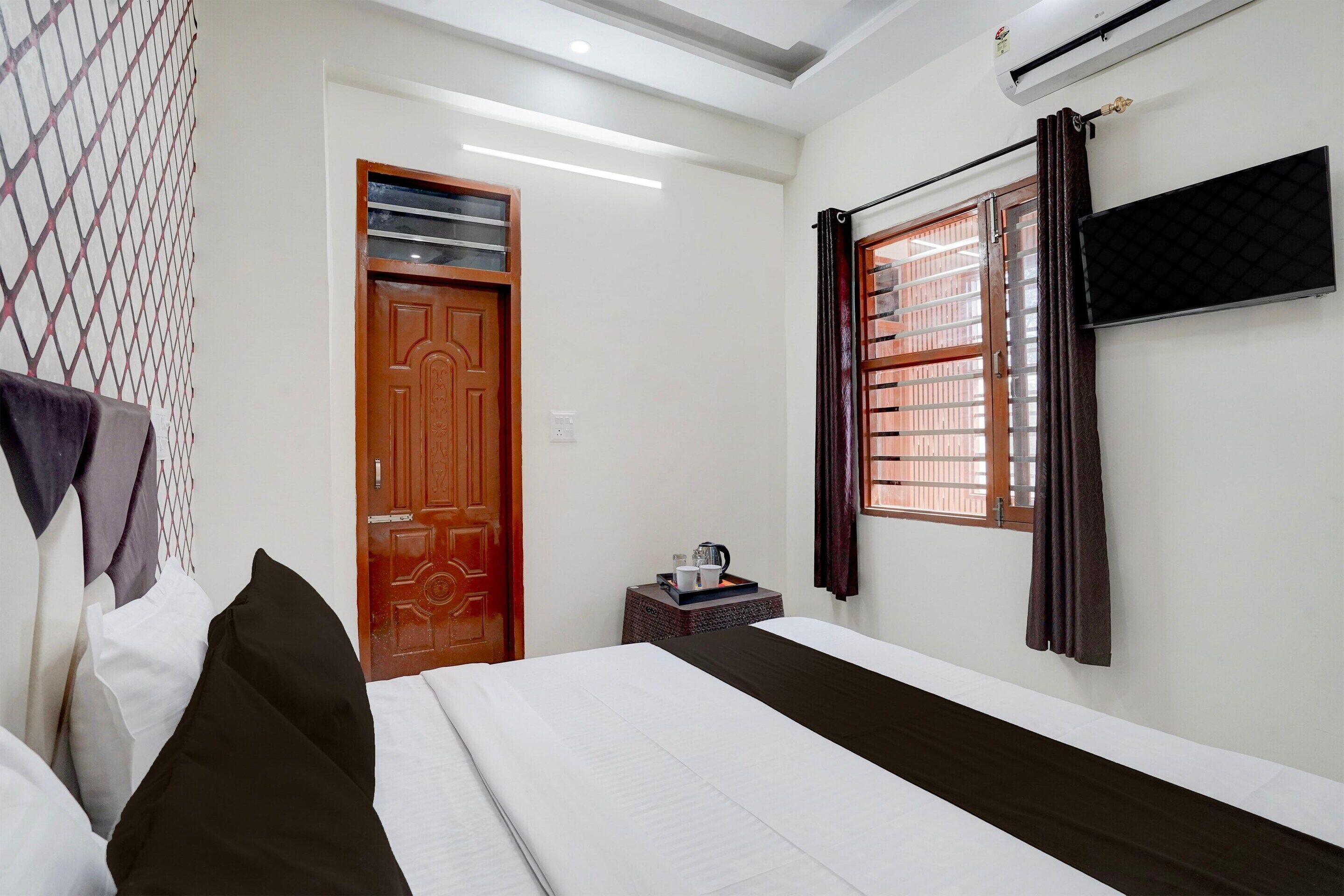 A hotel room with a bed, a small table with a tray, a window with curtains, and a wall-mounted air conditioner.