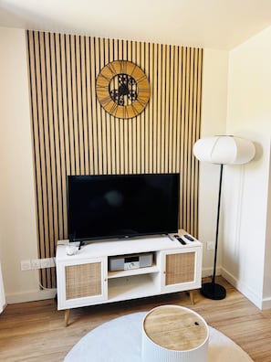 Un saló modern amb televisió de pantalla plana, paret de fusta, moble de televisió blanc i una làmpada de peu.