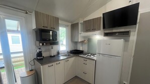 A compact kitchen with a gas stove, a microwave, a refrigerator, and a television mounted above the stove. - L'Eden - Mobile home 2 bedrooms 6 people - Swimming pool Air conditioning - Campsite 5⭐️ (Le Grau-du-Roi)