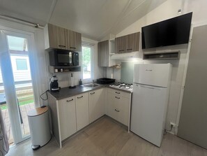 Een kleine keuken met een gasfornuis, een magnetron, een koelkast en een televisie die boven het fornuis is bevestigd.