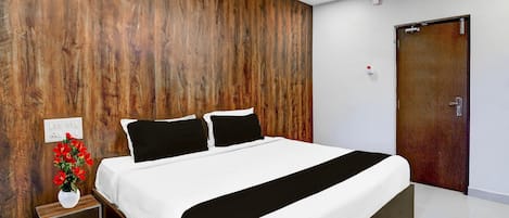 A bedroom with a wooden accent wall, a ceiling fan, a bed with white bedding, a nightstand with a vase of flowers, and a door.