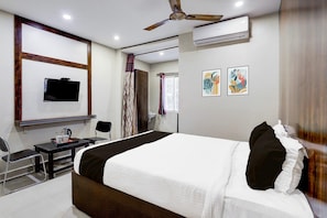 A hotel room with a bed, a desk with a chair, a television, an air conditioning unit, and two wall-mounted artworks. - Deluxe Renigunta Near Railway Station (Renigunta)