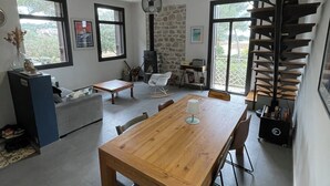 Une pièce spacieuse avec une table à manger en bois, une cheminée en pierre, un escalier en colimaçon et de grandes fenêtres offrant une vue imprenable.